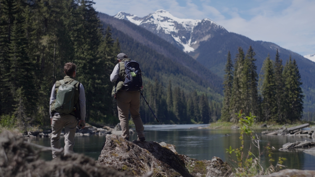 Two people stand on a rock by the Fraser River in Kanaka Bar territory.